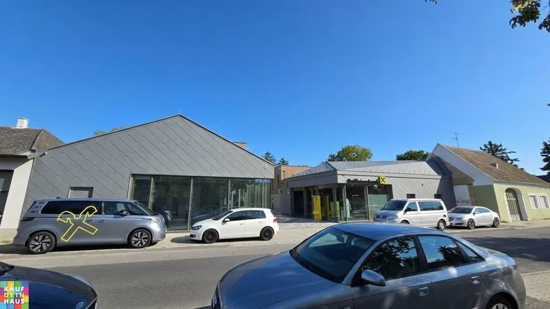 Ansicht der modernen Geschäftsgebäude an einer Straße mit parkenden Autos unter blauem Himmel.