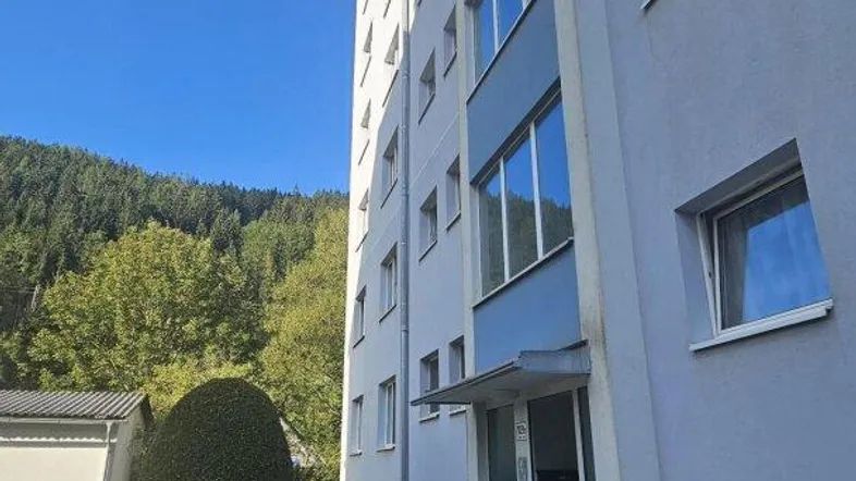Außenansicht eines Mehrfamilienhauses mit weißer Fassade, blauen Fenstern und gepflegtem Vorgarten.