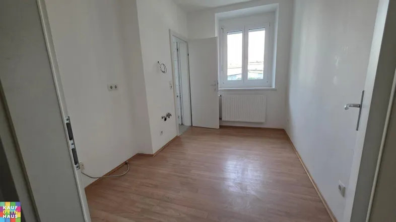 Helles Zimmer mit Laminatboden, weißen Wänden und einem Fenster, bereit zur individuellen Gestaltung.