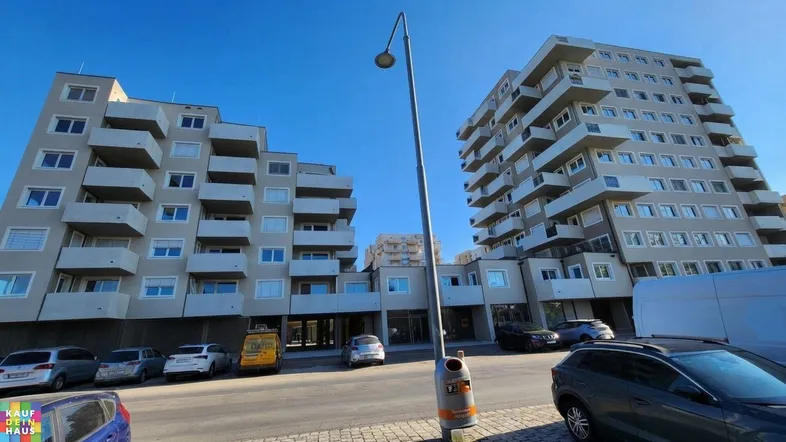 Außenansicht von zwei modernen Apartmentgebäuden mit gestuften Balkonen und Parkplätzen davor.