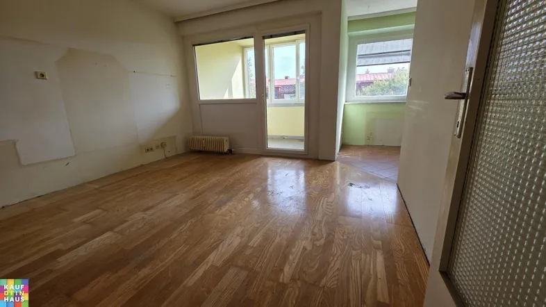 Geräumiges Zimmer mit Holzboden, Balkonzugang und Renovierungsbedarf, bietet Potenzial für individuelle Gestaltung.