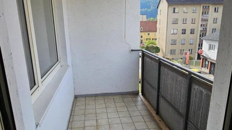 Heller Balkon mit Fliesenboden, Markise und weitem Blick auf die umliegenden Berge und Gebäude.