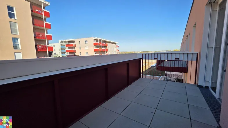 Geräumiger Balkon mit Fliesenboden und Blick auf umliegende Wohngebäude unter blauem Himmel.