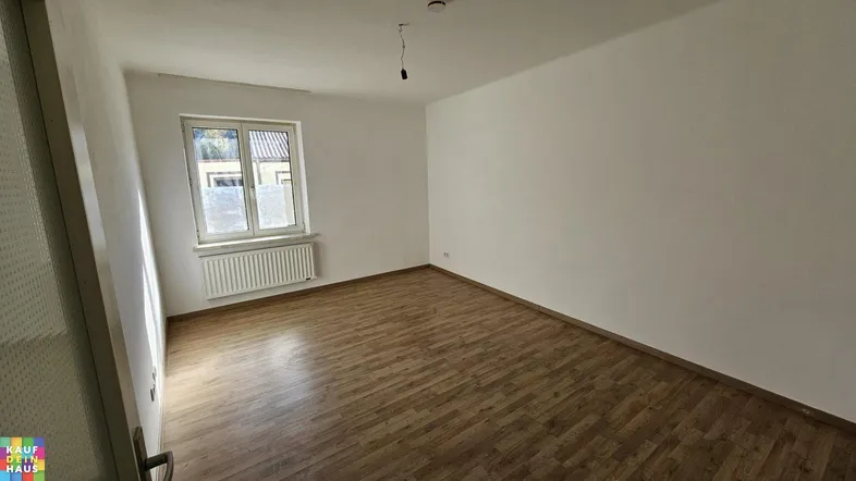 Helles, leeres Zimmer mit Laminatboden und Fenster, bereit zur individuellen Gestaltung.