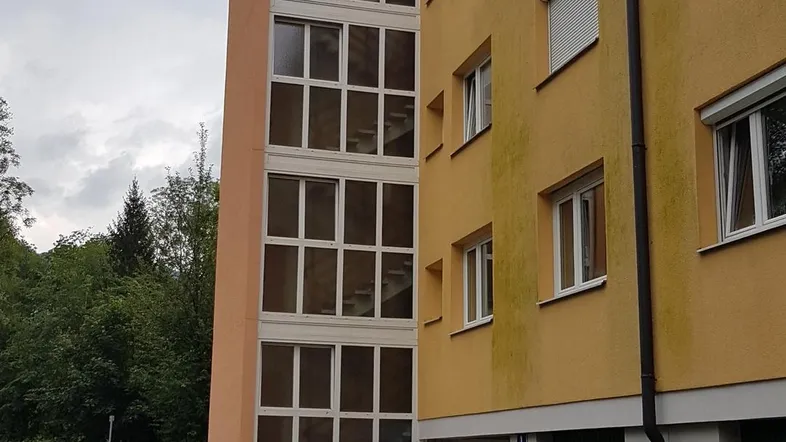 Mehrstöckiges Wohngebäude mit gelber Fassade, verglastem Treppenhaus und Garagen im Erdgeschoss.