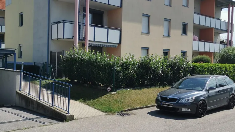 Mehrstöckiges Wohngebäude mit Balkonen und einem gepflegten Vorgartenbereich. Ein Auto parkt auf der Straße davor.