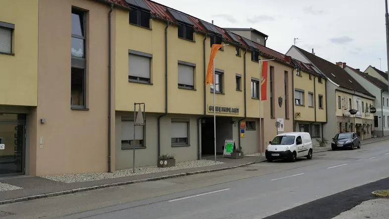 Mehrere Gebäude entlang einer Straße mit gelber Fassade und roten Dächern unter bewölktem Himmel.