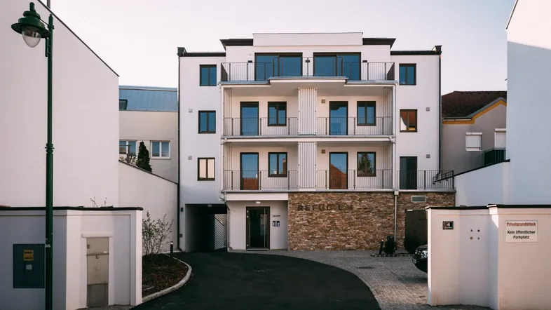 Modernes Mehrfamilienhaus mit weißer Fassade, Balkonen und Steinverkleidung im Eingangsbereich.