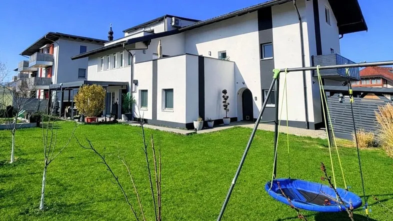 Großer Garten mit Rasenfläche und Kinderschaukel, ideal für Familien.