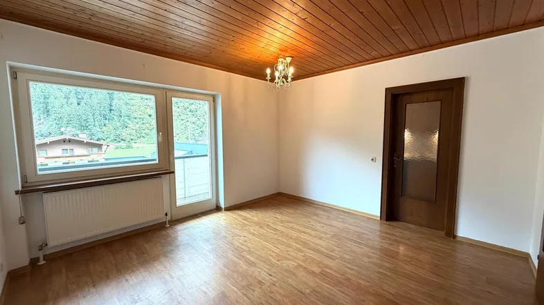 Helles Zimmer mit Holzbalkendecke, Parkettboden und Blick auf die umliegende Natur.