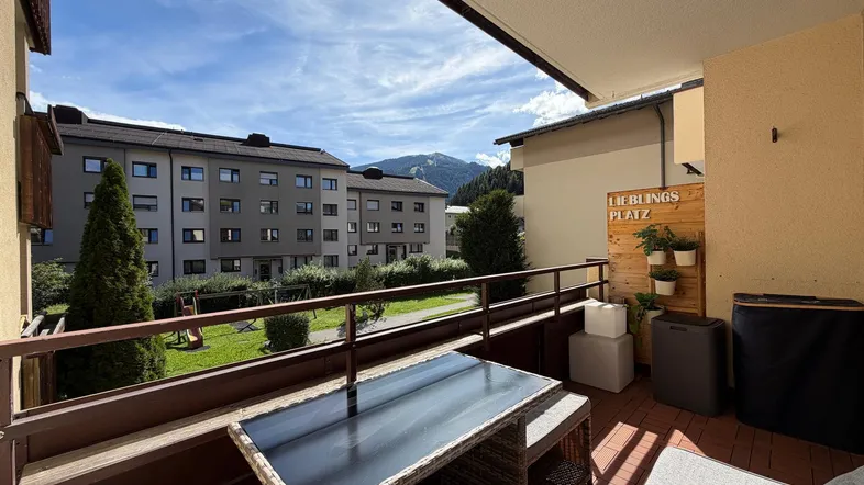 Geräumiger Balkon mit Sitzgelegenheiten und Bergblick, umgeben von Grünflächen und Wohngebäuden.