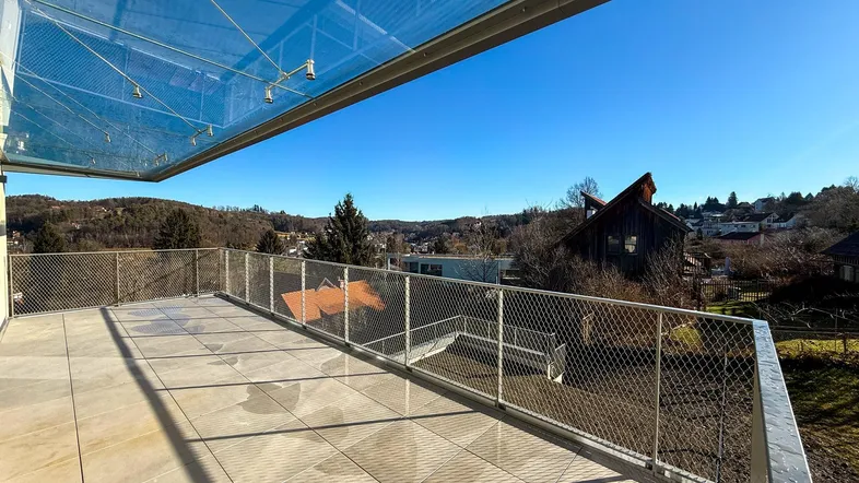Geräumige Terrasse mit Glasüberdachung und weitem Blick über die grüne Landschaft.