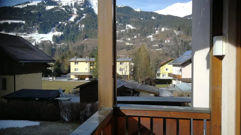 Balkon mit Holzbalken und Geländer bietet einen weiten Blick auf die schneebedeckten Berge und die umliegende Landschaft.