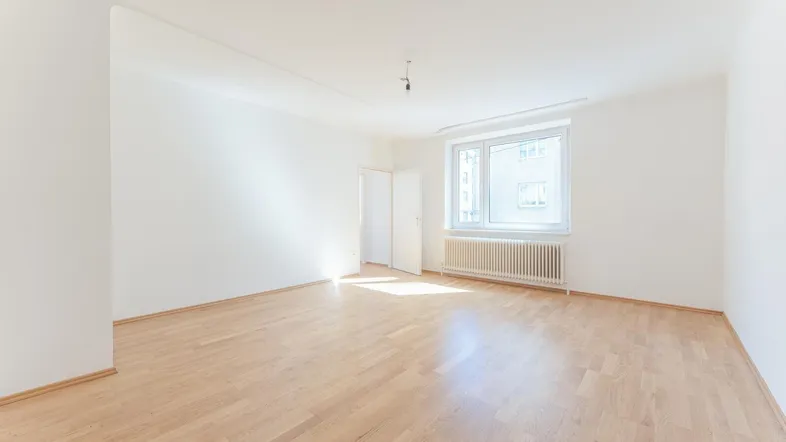Helles, leeres Zimmer mit Parkettboden und großen Fenstern, bereit zur individuellen Gestaltung.
