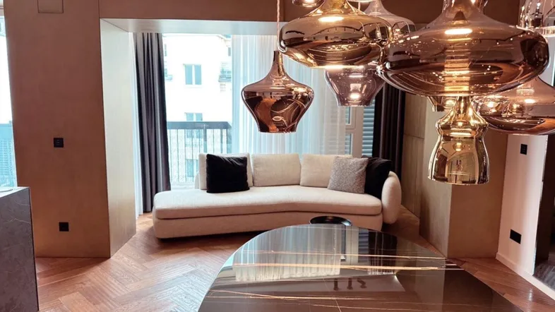 Modernes Wohnzimmer mit Fischgrätparkett, beigem Sofa und auffälligen Designer-Hängelampen.