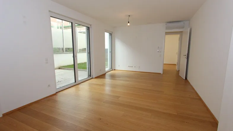 Heller, leerer Wohnraum mit Holzboden und großen Schiebetüren zum Außenbereich.