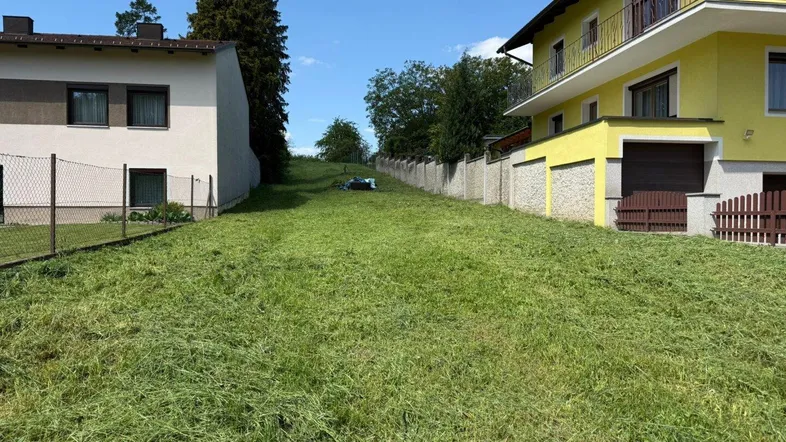 Großes, gepflegtes Grundstück mit Rasenfläche zwischen zwei Wohnhäusern unter blauem Himmel.