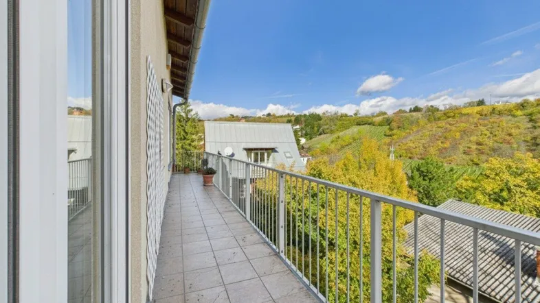 Langer Balkon mit Fliesenboden und einem weiten Blick über grüne Hügel und Dächer.