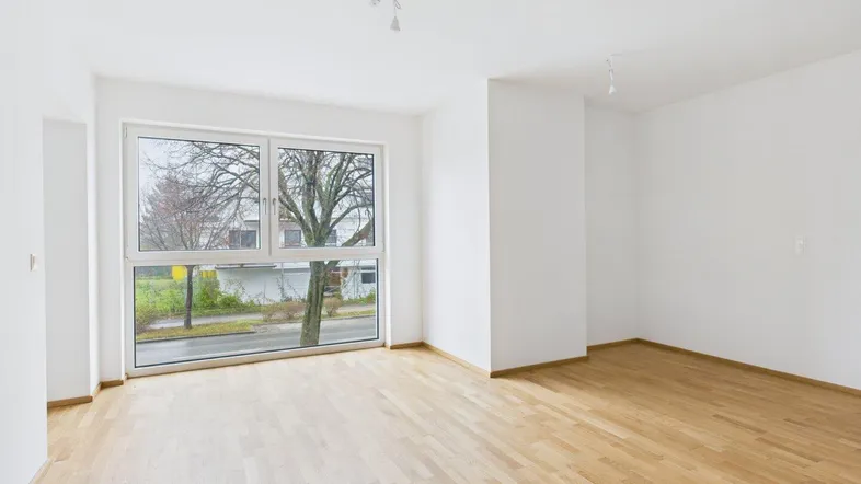 Helles, leeres Wohnzimmer mit großen Fenstern und Parkettboden, bereit zur individuellen Gestaltung.
