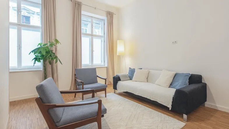 Helles Wohnzimmer mit bequemen Sitzmöbeln, Holzboden und großen Fenstern für viel Tageslicht.