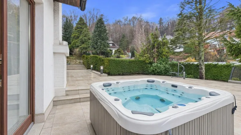 Entspannungsbereich im Freien mit Whirlpool auf einer gepflasterten Terrasse und grüner Umgebung.