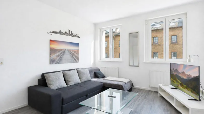 Helles Wohnzimmer mit modernem Sofa, Couchtisch aus Glas und Blick auf die gegenüberliegenden Gebäude.