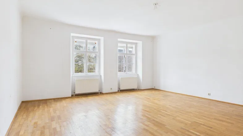 Helles, leeres Zimmer mit Parkettboden und zwei Fenstern, bereit zur individuellen Gestaltung.