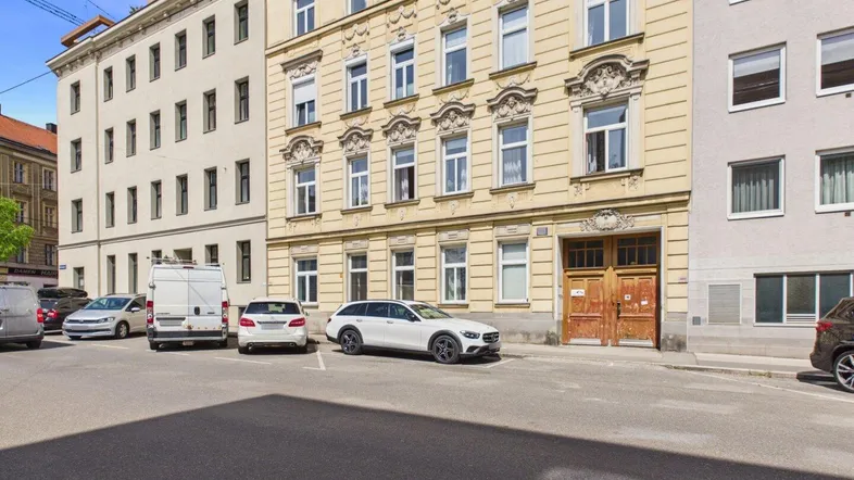 Fassade eines historischen Wohngebäudes mit mehreren Fenstern und geparkten Autos davor.