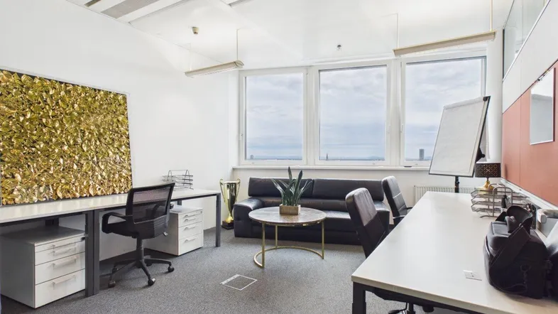Modernes Büro mit Schreibtischen, bequemer Sitzecke und großen Fenstern mit weitem Stadtblick.