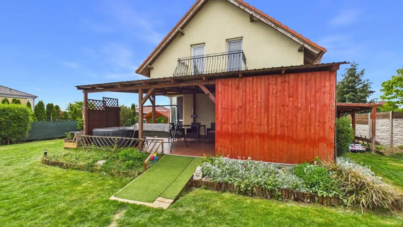 Ansicht des Hauses von hinten mit großem Garten, überdachter Terrasse und Balkon im Obergeschoss.