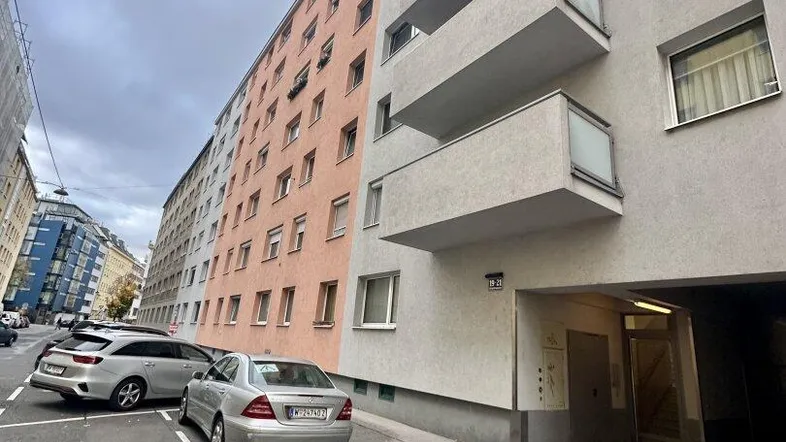 Straßenansicht eines Mehrfamilienhauses mit Balkonen und parkenden Autos davor.
