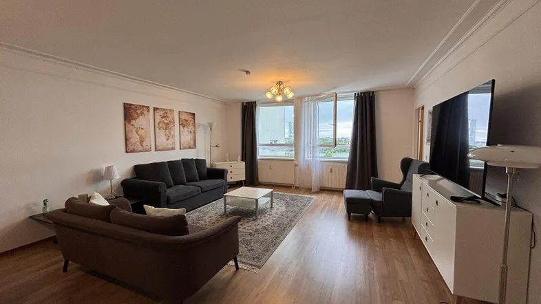 Geräumiges Wohnzimmer mit Holzboden, bequemen Sofas und Blick nach draußen durch große Fenster.