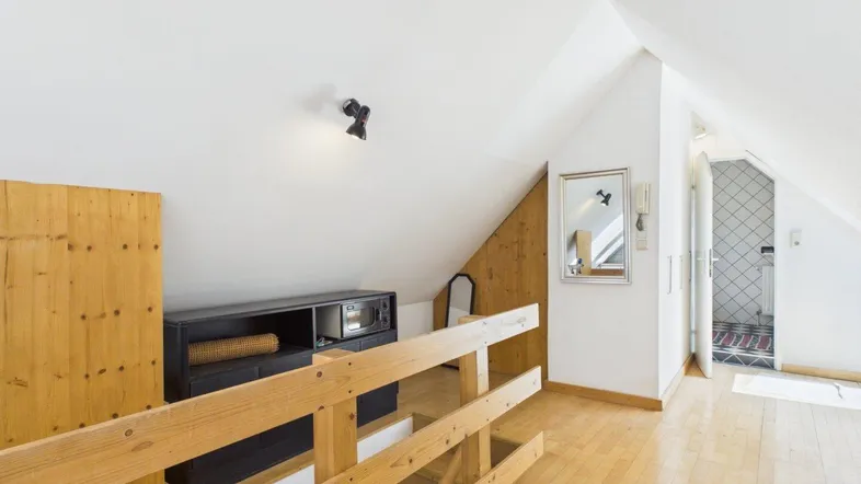 Heller Dachgeschossbereich mit Holzgeländer, Dachschrägen und Blick auf einen angrenzenden Raum.