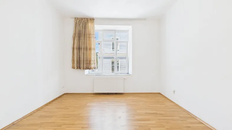 Helles, leeres Zimmer mit Parkettboden und einem Fenster mit Vorhang, bereit zur Einrichtung.
