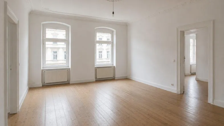 Helles, leeres Wohnzimmer mit hohen Decken, Stuckelementen und klassischem Dielenboden.