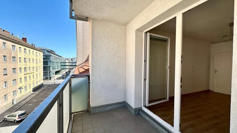 Heller Balkon mit Fliesenboden und Blick auf die Straße sowie angrenzende Gebäude.