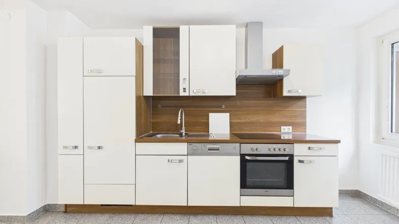 Helle Einbauküche mit weißen Schränken, Holzdekor und Fliesenboden in gutem Zustand.
