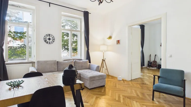 Heller Wohn- und Essbereich mit Fischgrätparkett, großen Fenstern und gemütlichem Sofa.