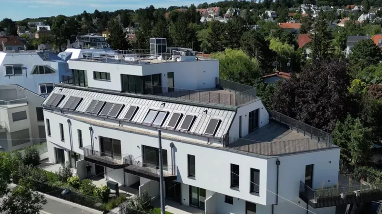 Moderne Wohnanlage mit Flachdach und Dachfenstern, umgeben von viel Grün.