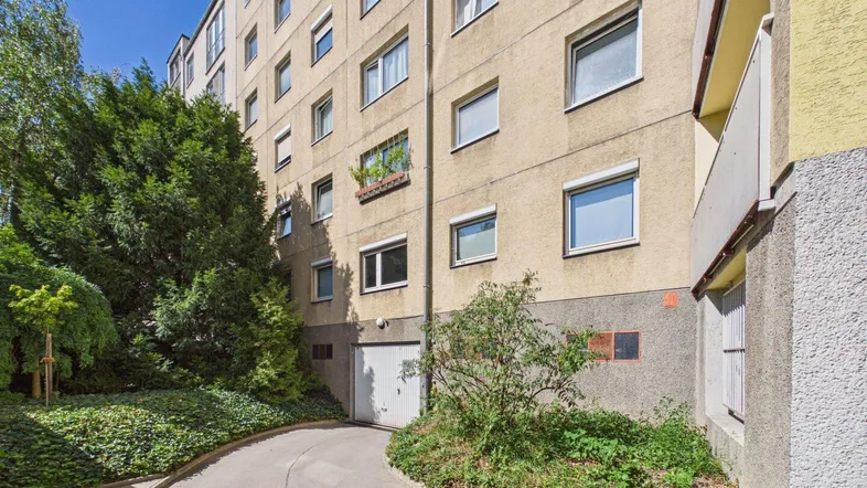 Mehrstöckiges Wohngebäude mit Zufahrt zur Tiefgarage und gepflegter Grünanlage.