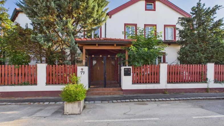 Vorderansicht des Hauses mit rotem Holzzaun und gepflegtem Eingangsbereich unter einem Vordach.