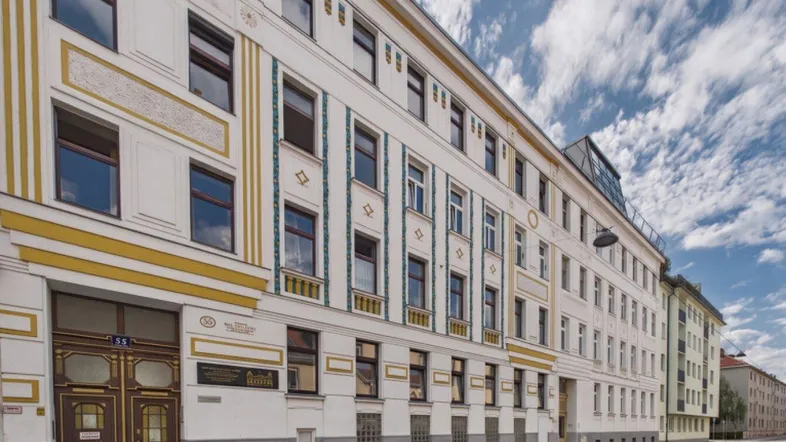 Historische Fassade eines Mehrfamilienhauses mit dekorativen Elementen und Fenstern.