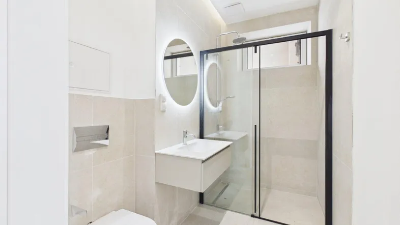 Modernes Badezimmer mit begehbarer Dusche, schwebendem Waschtisch und beleuchtetem Spiegel.