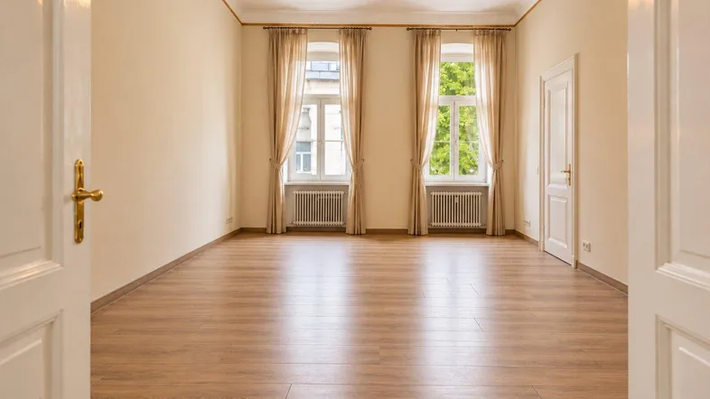 Helles, leeres Zimmer mit Parkettboden, hohen Fenstern und Deckenventilator, bereit zur individuellen Gestaltung.