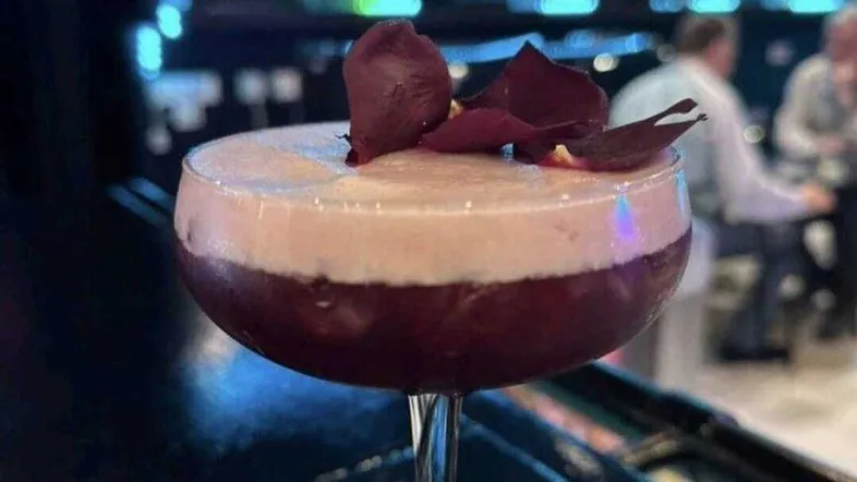 Ein kunstvoll zubereiteter Cocktail mit Schaum und Garnitur, serviert in einer Bar mit Neonbeleuchtung.