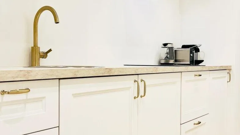 Moderne Küche mit weißen Schränken, goldfarbenen Armaturen und Dunstabzugshaube.
