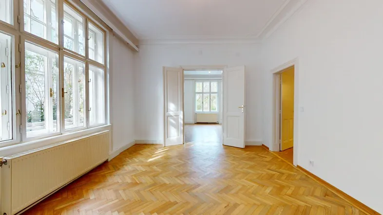 Helles Wohnzimmer in einem Altbau mit hohen Decken, Fischgrätparkett und großen Fenstern mit Blick ins Grüne.