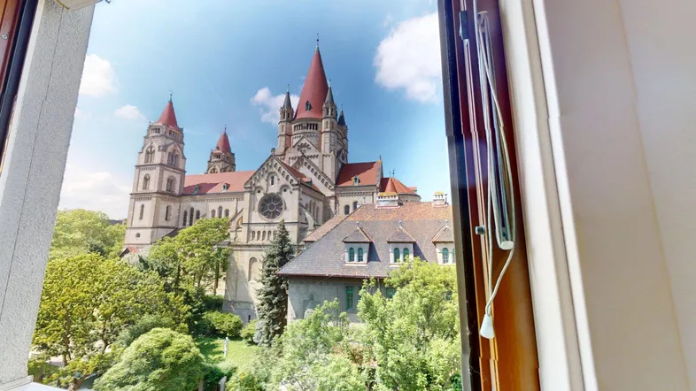 Blick aus dem Fenster auf eine beeindruckende Kirche mit roten Dächern und umliegenden grünen Bäumen.