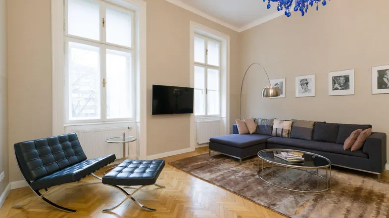 Geräumiges Wohnzimmer mit Fischgrätparkett, modernem Sofa und einem auffälligen blauen Kronleuchter.