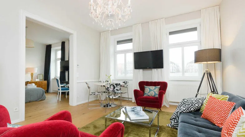 Helles Wohnzimmer mit Parkettboden, modernen Möbeln und einem Kronleuchter, offen zum Schlafzimmer.